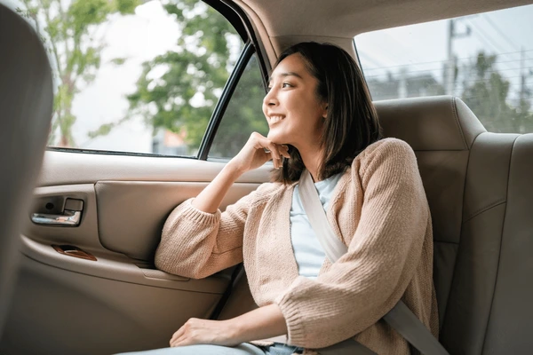 Smiling young woman looking out a car window while sitting in the backseat.